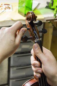 The best position to tune your violin: sit, put the instrument on your lap, grip it tightly and turn the pegs.